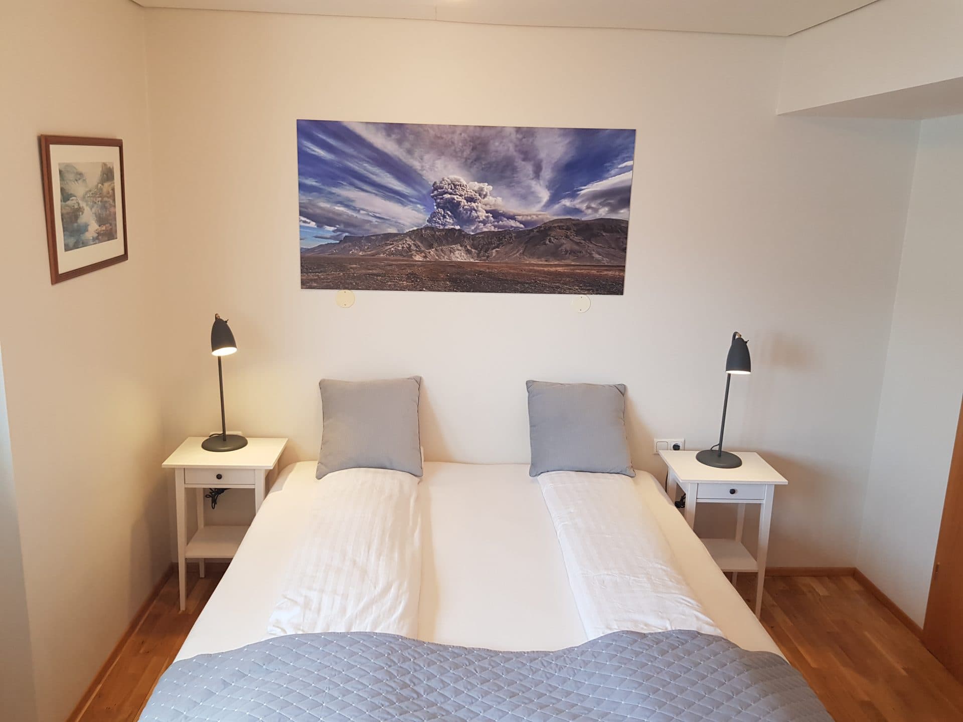 Double room with white bedding, bedside lamps and a print of an erupting volcano